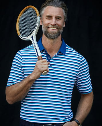 Man wearing the Forge Polo Multi Stripe in Chambers by Cutter and Buck, holding a racket