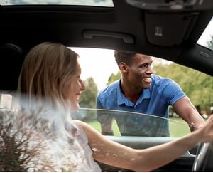 Woman in a car talking to a man wearing a Cutter and Buck men's blue golf polo.