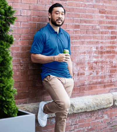 Man wearing a blue Cutter and Buck polo drinking a beer outside