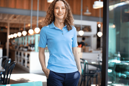 Woman at a cafe wearing Cutter & Buck Virtue Eco Pique Recycled Womens Polo