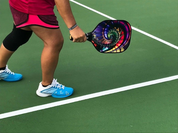 A pickleball player holding a colorful spiral styled pickleball player on a court